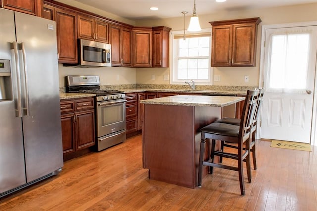 kitchen featuring stainless steel appliances, a kitchen island, a sink, light wood-style floors, and pendant lighting