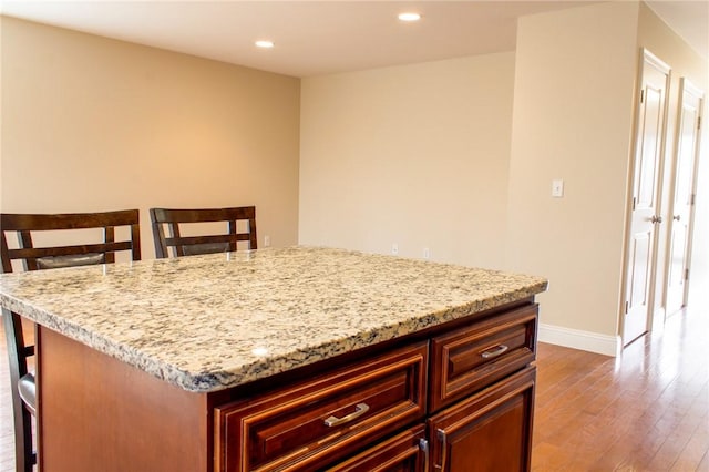 kitchen featuring recessed lighting, baseboards, light stone countertops, dark wood-style floors, and a kitchen bar