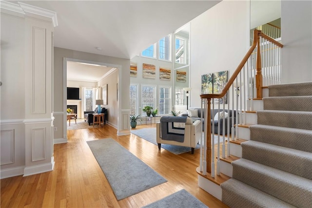 foyer featuring light wood finished floors, decorative columns, a fireplace, and stairway