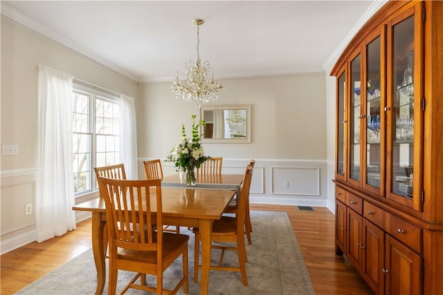 dining room featuring visible vents, wood finished floors, crown molding, a chandelier, and a decorative wall