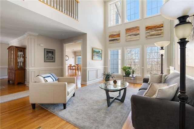 living area with a decorative wall, wood finished floors, ornamental molding, wainscoting, and ornate columns