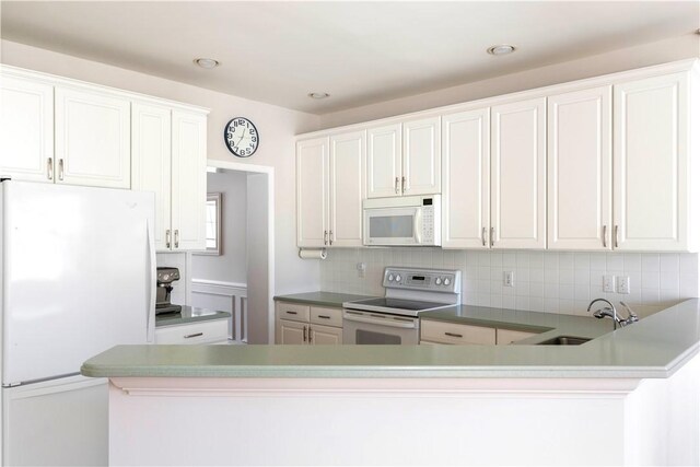 kitchen with backsplash, white cabinets, a sink, white appliances, and a peninsula