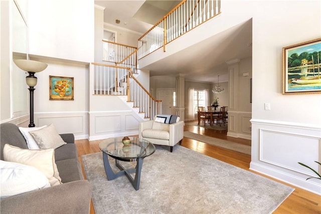 living area with a decorative wall, wood finished floors, stairway, decorative columns, and crown molding