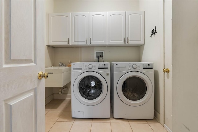 clothes washing area with light tile patterned floors, washer and clothes dryer, a sink, and cabinet space