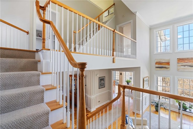 stairs featuring baseboards, a high ceiling, wood finished floors, and crown molding