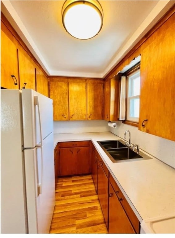 kitchen with brown cabinetry, freestanding refrigerator, light countertops, light wood-style floors, and a sink