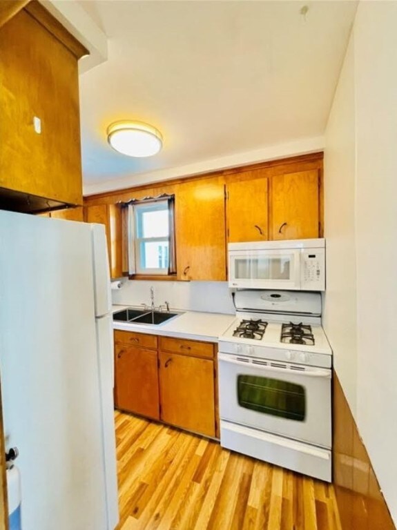 kitchen featuring white appliances, brown cabinetry, light wood-style floors, and light countertops