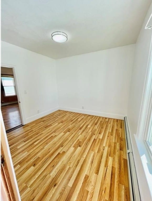 unfurnished room with light wood-style floors, a baseboard radiator, and baseboards