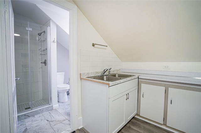 bathroom with a stall shower, toilet, marble finish floor, vaulted ceiling, and vanity