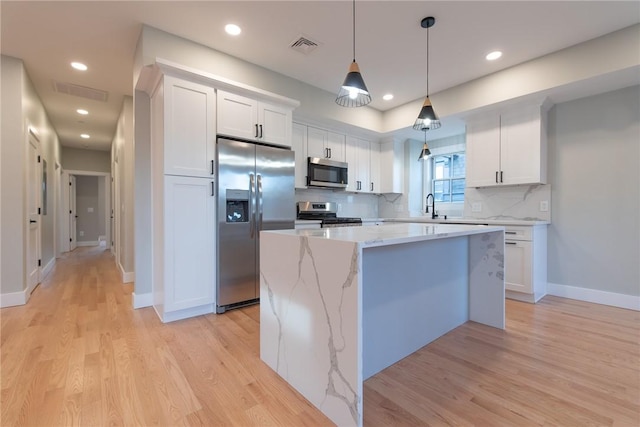 kitchen with stainless steel appliances, light wood finished floors, a kitchen island, and white cabinetry