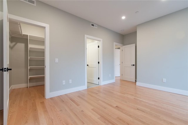 unfurnished bedroom with light wood finished floors, visible vents, baseboards, a walk in closet, and a closet