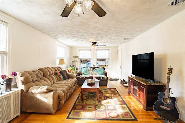 living room featuring a textured ceiling, ceiling fan, visible vents, light wood-style floors, and radiator heating unit