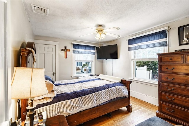 bedroom featuring visible vents, a ceiling fan, a textured ceiling, light wood-type flooring, and baseboards