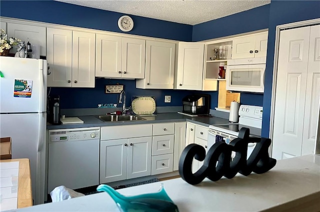 kitchen featuring a textured ceiling, white appliances, a sink, and white cabinetry