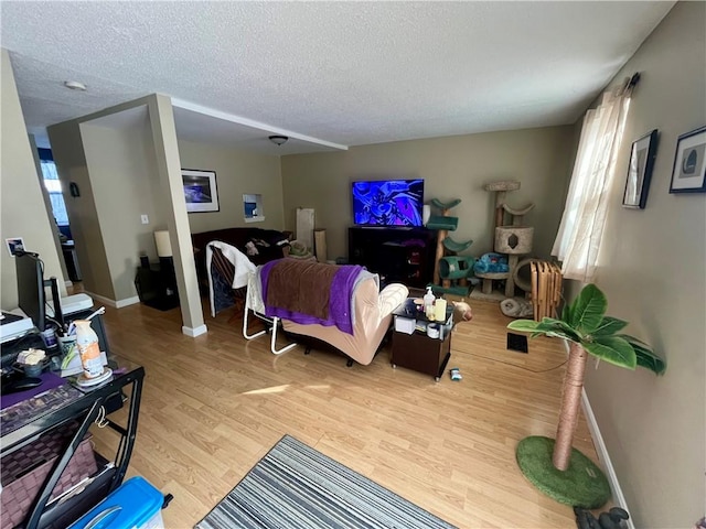 living area featuring a textured ceiling, light wood finished floors, and baseboards