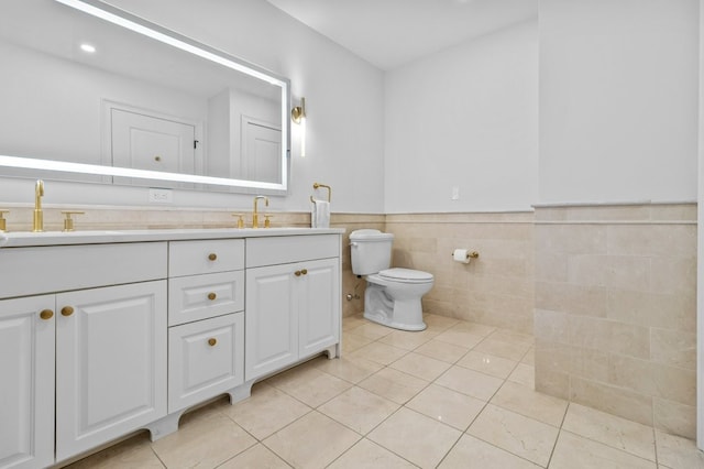 bathroom featuring toilet, a wainscoted wall, a sink, tile patterned floors, and double vanity