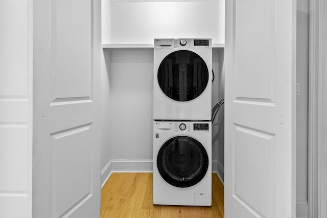 laundry area with stacked washer and dryer, laundry area, light wood-style floors, and baseboards