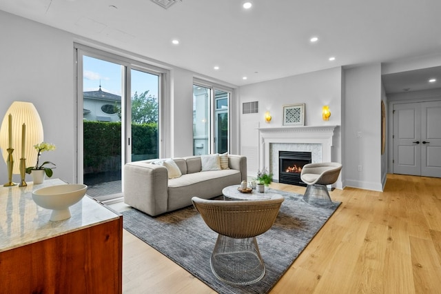 living room featuring recessed lighting, a premium fireplace, visible vents, baseboards, and light wood finished floors