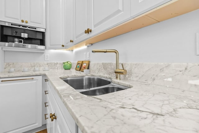 kitchen with light stone counters, white cabinets, and a sink