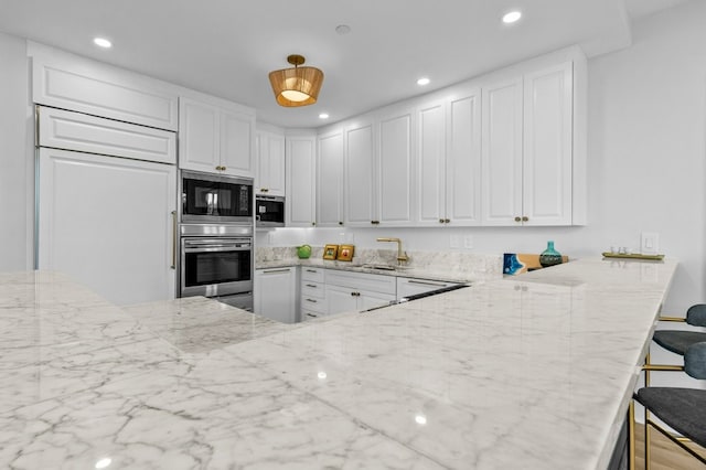 kitchen featuring light stone countertops, white cabinetry, a sink, and built in appliances