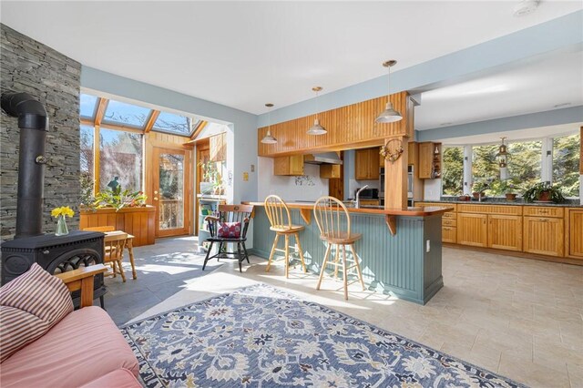 kitchen with a breakfast bar area, a wood stove, ventilation hood, pendant lighting, and a sink