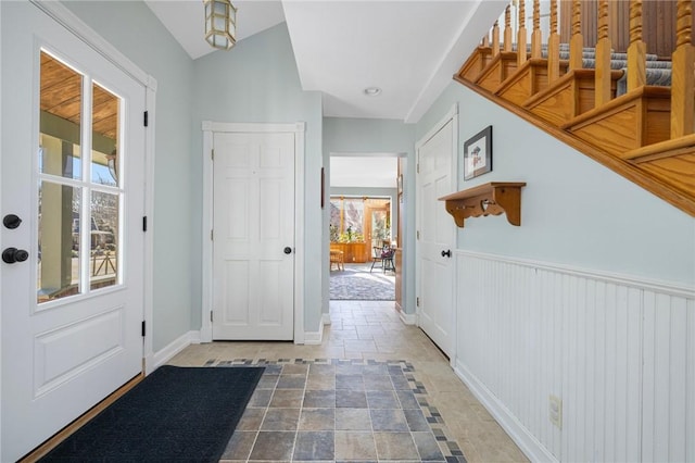 foyer entrance with lofted ceiling, a wainscoted wall, baseboards, and stone finish floor