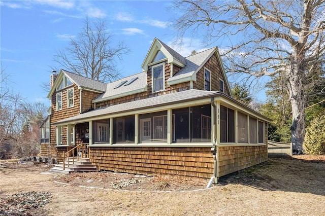 view of front of property with a sunroom, roof with shingles, and a chimney