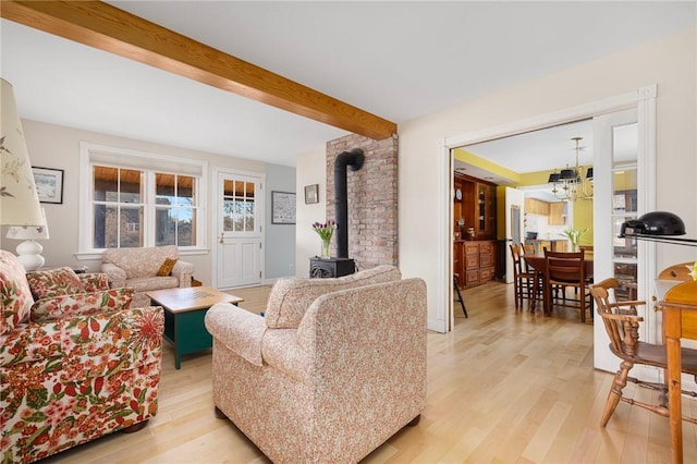 living room with a wood stove, light wood finished floors, a chandelier, and beamed ceiling