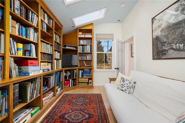 living area with lofted ceiling with skylight, bookshelves, and wood finished floors