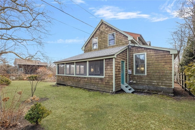 rear view of house featuring a yard, roof with shingles, and a sunroom