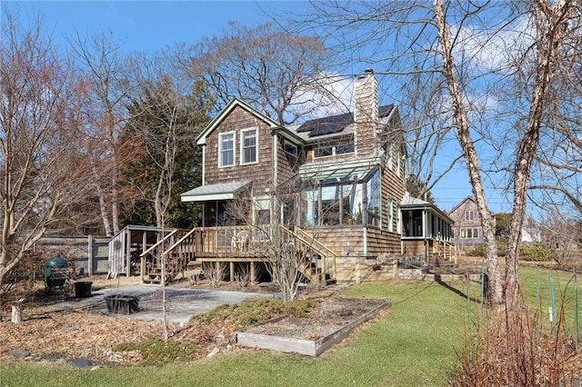 rear view of house with solar panels, a sunroom, a chimney, stairway, and a deck