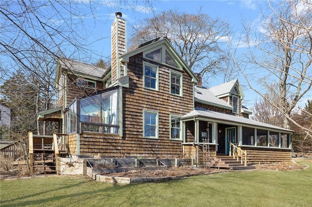 view of front of house with roof with shingles, a chimney, a front yard, and a sunroom