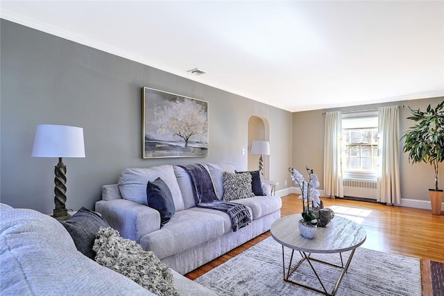 living room with radiator heating unit, visible vents, arched walkways, and light wood finished floors