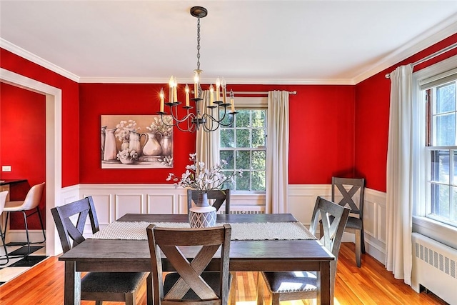 dining area with radiator, a wainscoted wall, wood finished floors, crown molding, and a notable chandelier