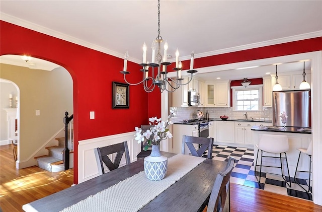 dining room with arched walkways, ornamental molding, wood finished floors, and an inviting chandelier