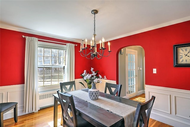 dining space with light wood-style floors, arched walkways, and a wainscoted wall