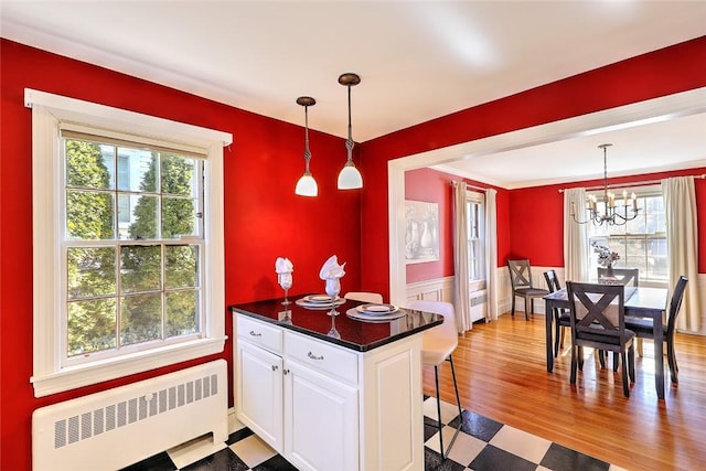 kitchen featuring white cabinets, radiator, dark countertops, a wainscoted wall, and pendant lighting