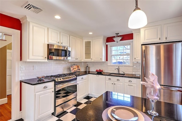 kitchen featuring light floors, dark countertops, visible vents, appliances with stainless steel finishes, and a sink