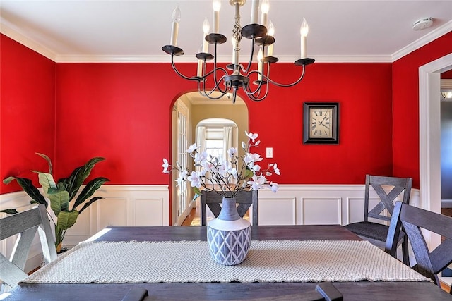 dining area with arched walkways, a decorative wall, a wainscoted wall, an inviting chandelier, and crown molding