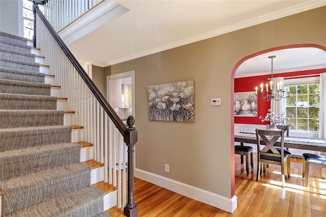 stairs featuring baseboards, arched walkways, ornamental molding, wood finished floors, and a chandelier