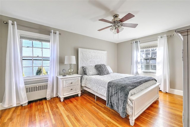 bedroom with radiator, light wood finished floors, multiple windows, and a ceiling fan