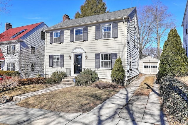 colonial home featuring an outbuilding, concrete driveway, a chimney, and a garage