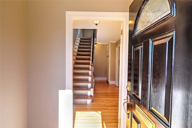 foyer entrance with stairs, baseboards, wood finished floors, and ornamental molding