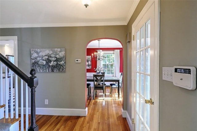 entrance foyer featuring baseboards, arched walkways, ornamental molding, wood finished floors, and stairs