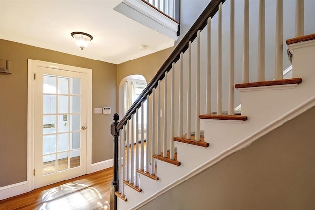 interior space featuring baseboards, ornamental molding, arched walkways, and wood finished floors