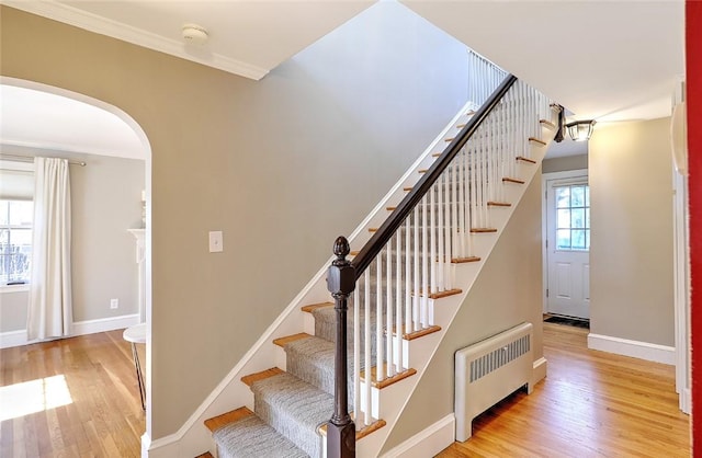 stairs with arched walkways, radiator heating unit, wood finished floors, and baseboards