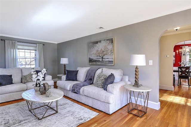 living area with arched walkways, crown molding, visible vents, light wood-type flooring, and baseboards