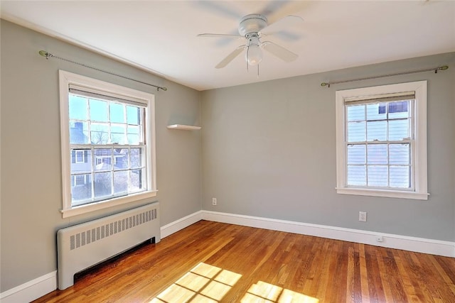 unfurnished room featuring radiator heating unit, wood finished floors, a ceiling fan, and baseboards