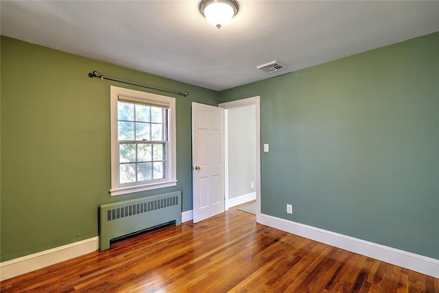 unfurnished room with baseboards, radiator heating unit, visible vents, and wood finished floors