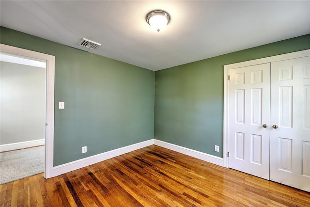 unfurnished bedroom featuring a closet, wood finished floors, visible vents, and baseboards